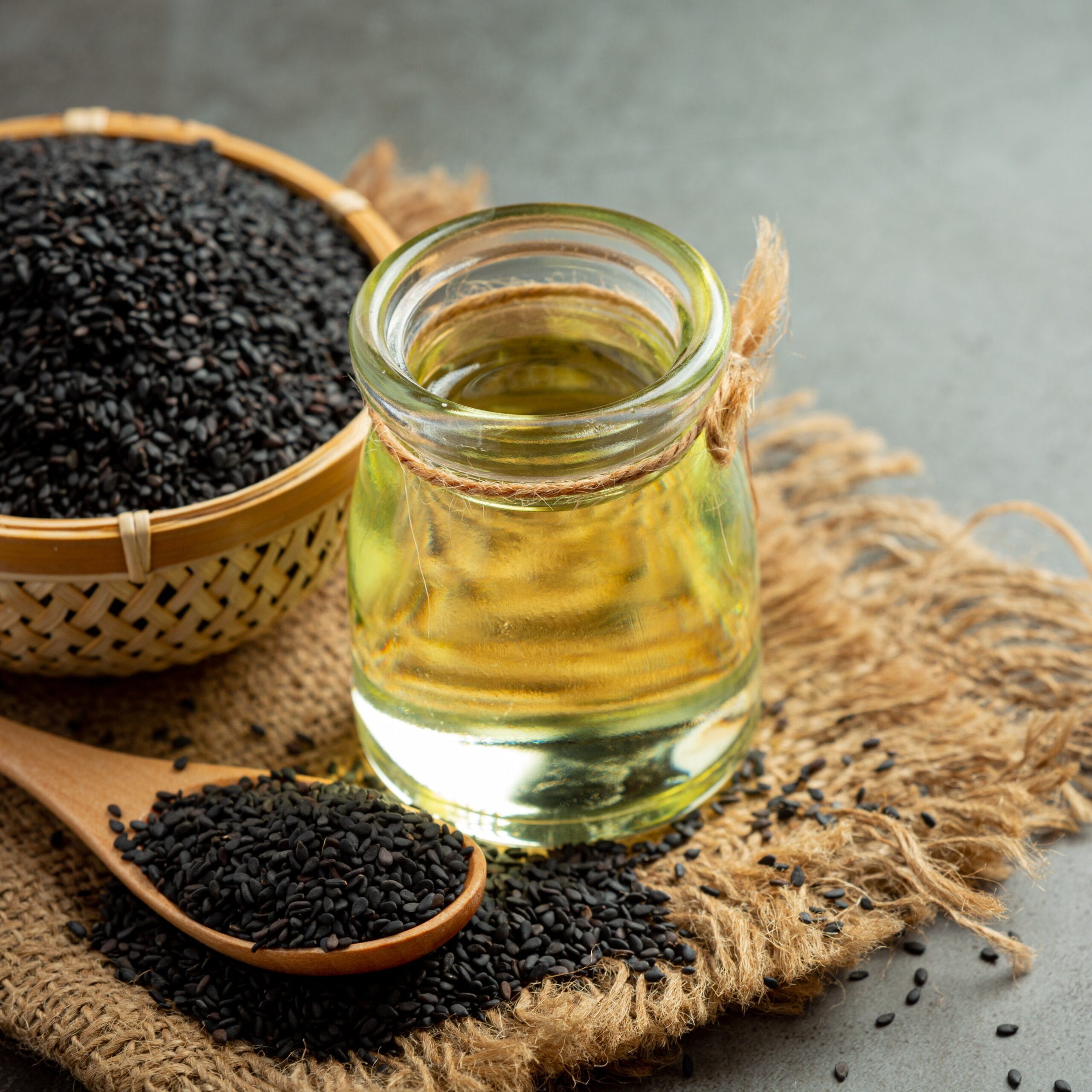 Sesame oil and raw black sesame seeds on dark background